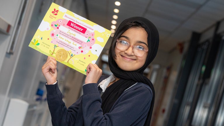 A young girl in headscarf and wearing glasses hold a certificate.